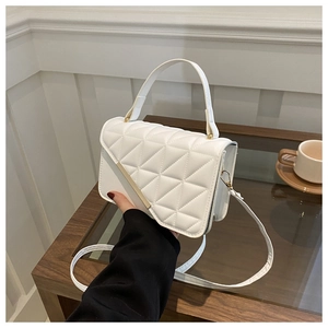 Detail shot of a white quilted crossbody bag with gold metal trim on a wooden table
