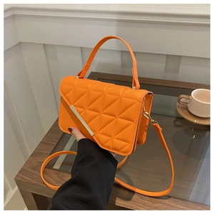 Detail of bright orange quilted PU leather small square bag with golden metal trim
