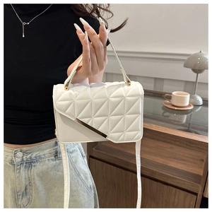Close-up of white quilted handbag with gold accents held by a model in a cozy room