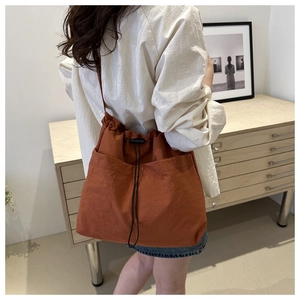 Detail of the rust orange drawstring tote bag shown with a model in a cozy indoor setting