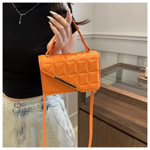 Detail view of orange quilted crossbody bag with metal bar and top handle on model