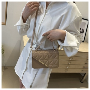 Detail of elegant beige quilted square handbag with minimalist gold metal bar and top handle