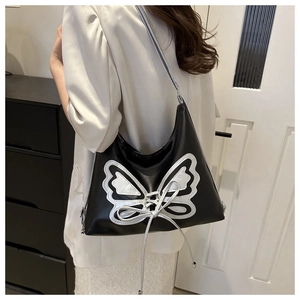 Detail of a black leather shoulder bag with a silver butterfly patch and bow on a model