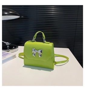 Detail of neon green square bag with silver metallic bow and top handle on a table