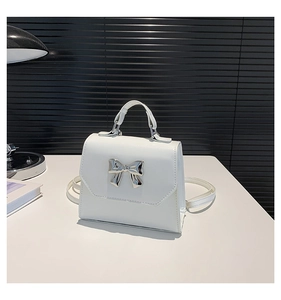 Detail of white mini crossbody bag featuring a silver bow-knot metal ornament on the flap