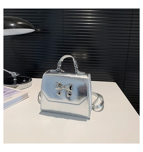 Close-up of a silver metallic bow square bag with glossy texture and top handle