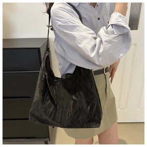 Détail du sac cabas noir à texture plissée brillante porté à l'épaule par le mannequin