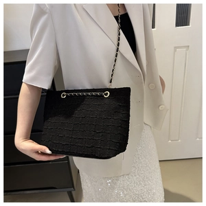 Détail de la texture en tweed noir et de la bandoulière en chaîne dorée du sac seau