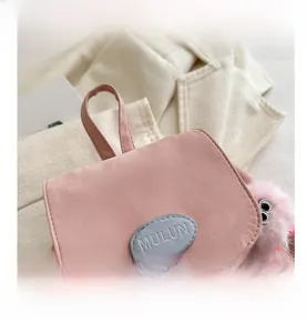 Close-up of pink bucket bag flap with brand logo and cute plush ball accessory