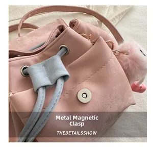 Detail of pink bucket bag featuring magnetic snap closure and plush pompom charm