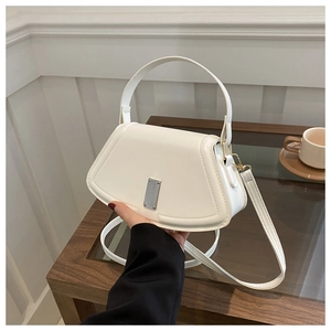 Close-up of cream white trapezoid crossbody bag with silver lock on a wooden table