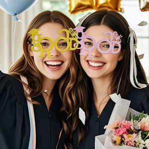 Glitter graduation party glasses with Grad letters and cap shown on a model in graduation gown