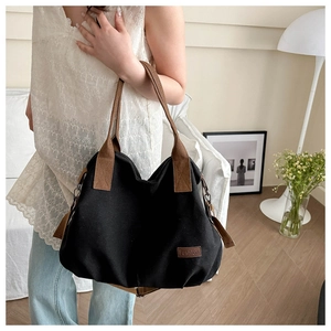 Detail of black canvas tote bag with brown straps and Fashion label in a home setting