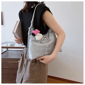 Detail of silver metallic underarm bag featuring a metal bow and cartoon charm