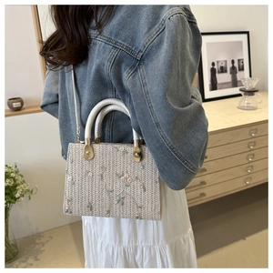 Detailed close-up of beige straw handbag with pink and green floral embroidery patterns