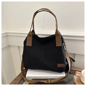 Detail of black canvas tote bag with brown webbing handles and Fashion leather patch