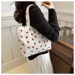 Close-up of a white corduroy tote bag featuring a cute red strawberry print pattern