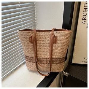 Detail of woven straw tote bag with brown leather handles and striped cutout patterns