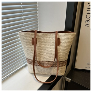 Detailed shot of beige woven tote bag with brown straps and patterned trim on windowsill