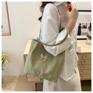 Detail of light green tote bag with pleated texture and silver butterfly ornament