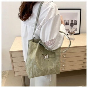 Detailed view of light green tote bag with metallic butterfly logo and wrinkled fabric