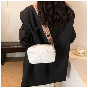 Detail of white quilted crossbody bag with stylish geometric woven wide strap and silver clips