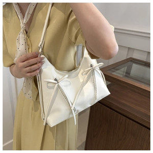 Close-up of white PU leather underarm bag featuring side ribbon bow and zipper details