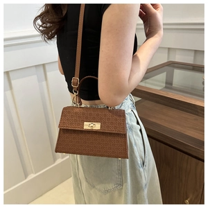 Detail view of brown textured crossbody bag with gold turn-lock on a fashion model