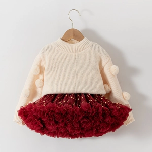 Detail of cream knit sweater with pom-poms and red tulle skirt with gold star prints
