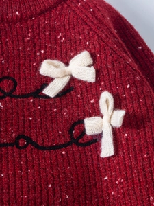 Detailed macro view of dark red knit sweater featuring white bows and wave embroidery