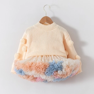 Detailed view of girl's knit dress featuring soft pom-poms and colorful layered tulle