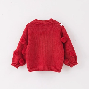 Detailed view of red chunky knit children's sweater with soft 3D pom-poms on the sleeves