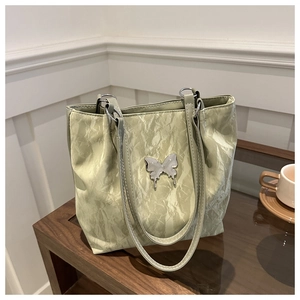 Close-up of a light green pleated tote bag featuring a silver metal butterfly ornament
