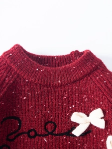 Detailed view of red knitted sweater with white speckles and a cute white bow accent