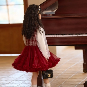 Vista trasera de niña en vestido de princesa de tweed rojo con falda de tul y diadema de perlas