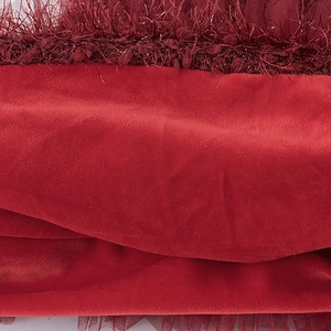 Primer plano del vestido de terciopelo rojo para niña con tela lujosa y borde de plumas