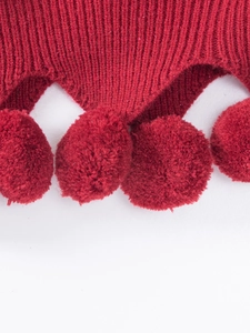 Close-up of red knitted fabric with matching plush pom-poms for festive skirt outfit