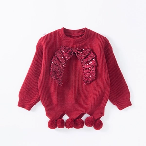 Close-up of red knit sweater with sequined bow detail and decorative pom-poms on the hem