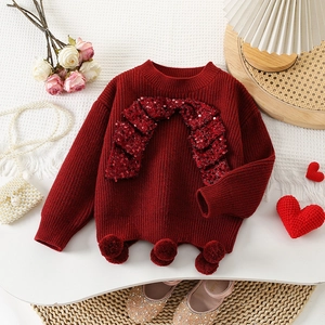 Detail of red knit sweater featuring sequin patterns and plush pom-poms for kids