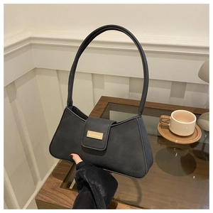 Detail of a black matte shoulder bag with a gold rectangular metal buckle on a coffee table