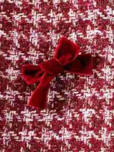 Primer plano detallado de un lazo de terciopelo rojo sobre tela de tweed roja