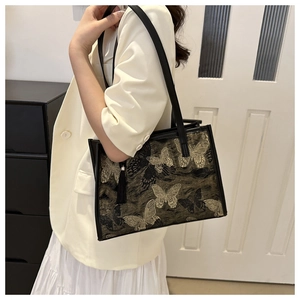 Detail of black tote bag with gold butterfly embroidery and elegant side tassel fringe