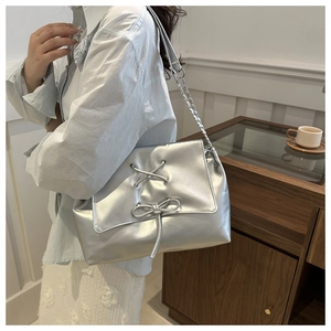 Detail of silver tote bag featuring decorative lace-up bow and metallic chain strap