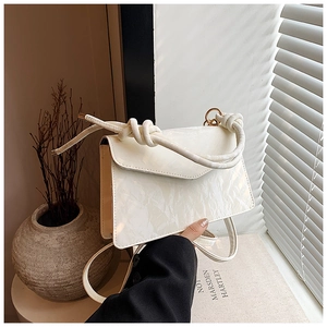 Detail of cream white glossy leather handbag featuring textured pleats and knotted strap