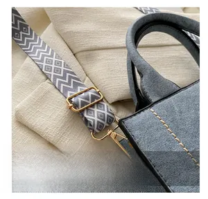 Detail van blauwe matte handtas met geometrische geweven riem en gouden metalen gespen
