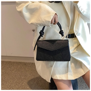 Close-up of black crossbody bag with knotted handle and elegant gold hardware detail