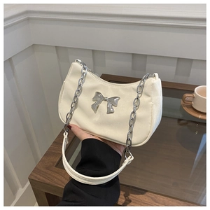 Detail of creamy white crescent handbag with silver bow charm and chain strap