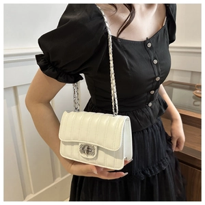 Detail of white quilted crossbody bag with rhinestone clasp and silver chain strap