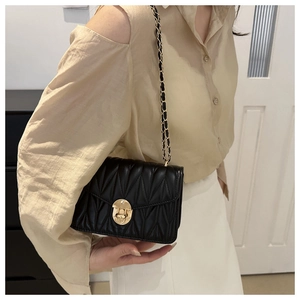 Detail of black quilted leather crossbody bag with elegant gold round lock and chain strap