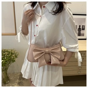 Detailed view of glossy pink bow handbag worn over the shoulder with striped shirt dress